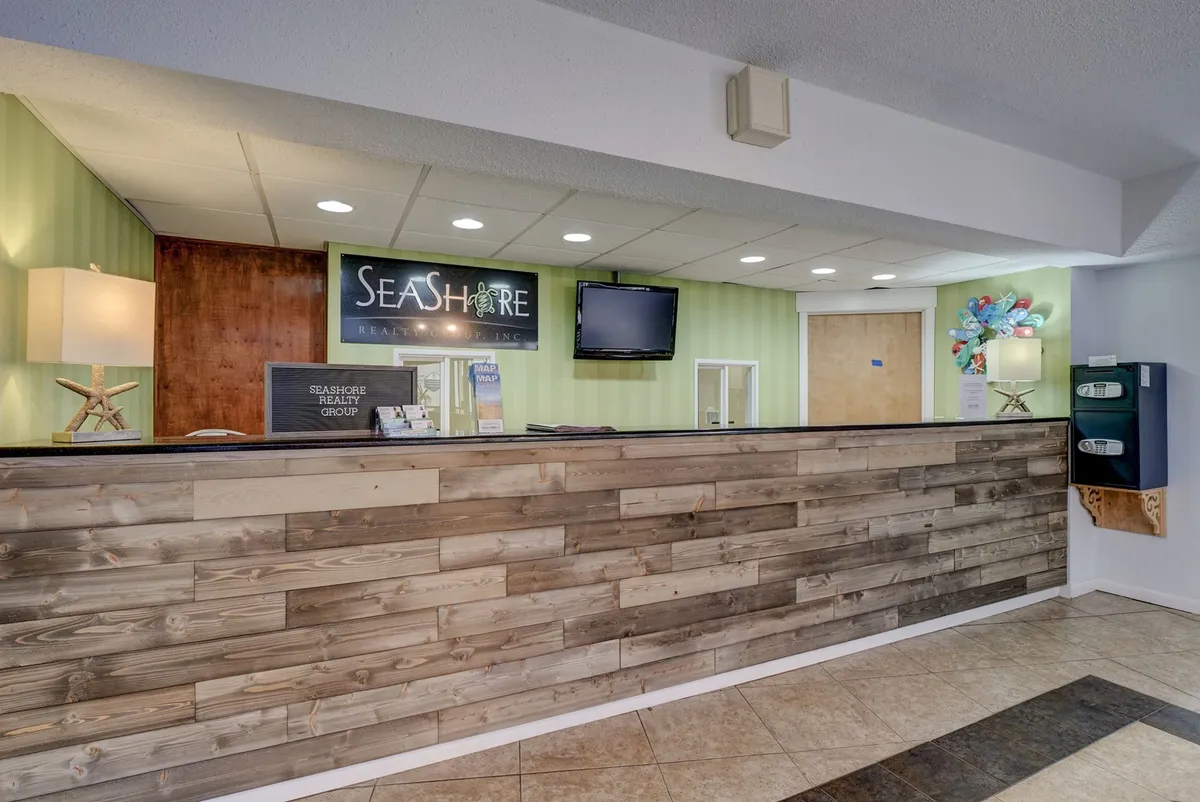 This image shows a welcoming reception area with a modern wood-paneled reception desk, a Seashore Realty sign, and warm lighting. The space is inviting, with clear signage and a friendly atmosphere that puts guests at ease upon arrival.