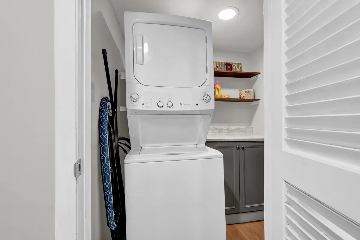 A dedicated laundry area featuring a washer and dryer unit, shelves stocked with cleaning supplies, and cabinetry for storage. The space is organized and functional, conveying home-like practicality.