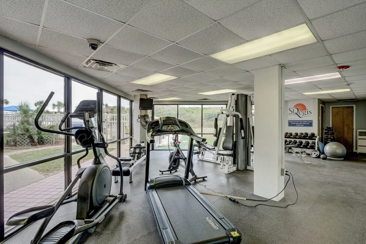 A bright, modern interior fitness center featuring up-to-date exercise equipment such as treadmills, ellipticals, and weight machines. Large windows flood the space with natural light, creating a motivating workout environment.