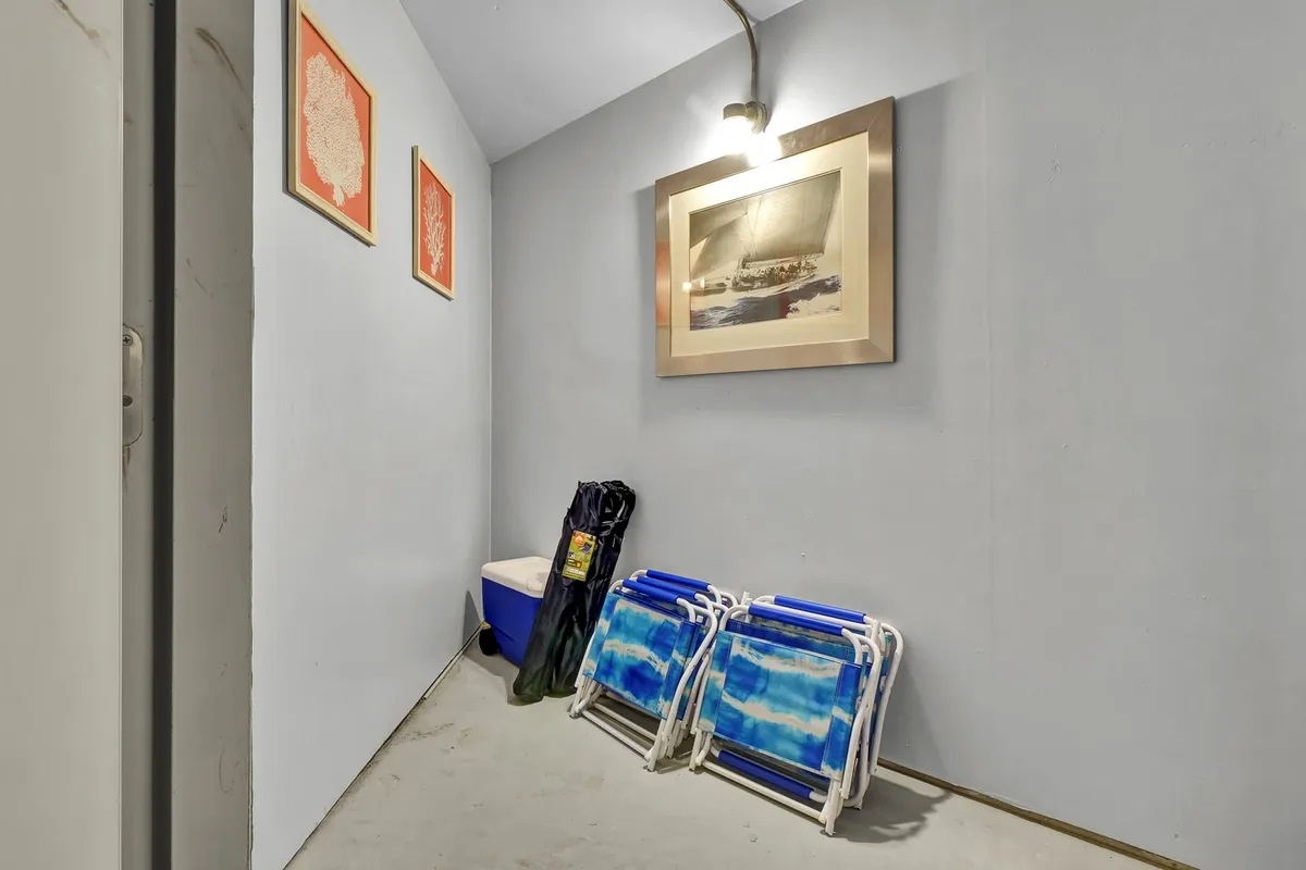A casual storage nook with beach chairs, a cooler, and framed artwork, suggesting a spot for stowing beach equipment and preparing for seaside adventures.