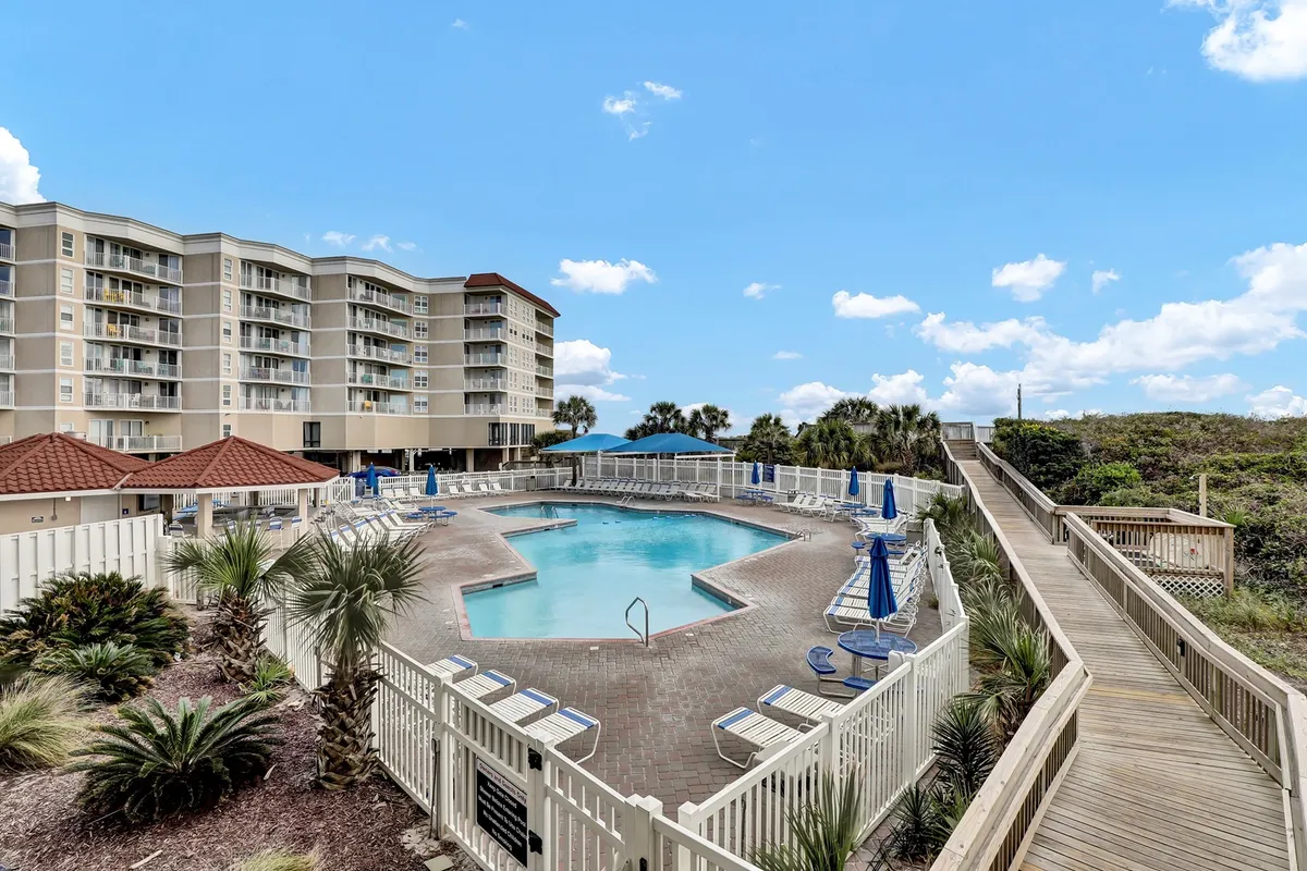 The exterior image showcases a sparkling saltwater pool surrounded by tall palm trees, with the modern facade of the St Regis condo building and a spacious deck area. The scene is bathed in the warm glow of sunset, suggesting a serene atmosphere perfect for relaxing, swimming, or gathering with friends and family.