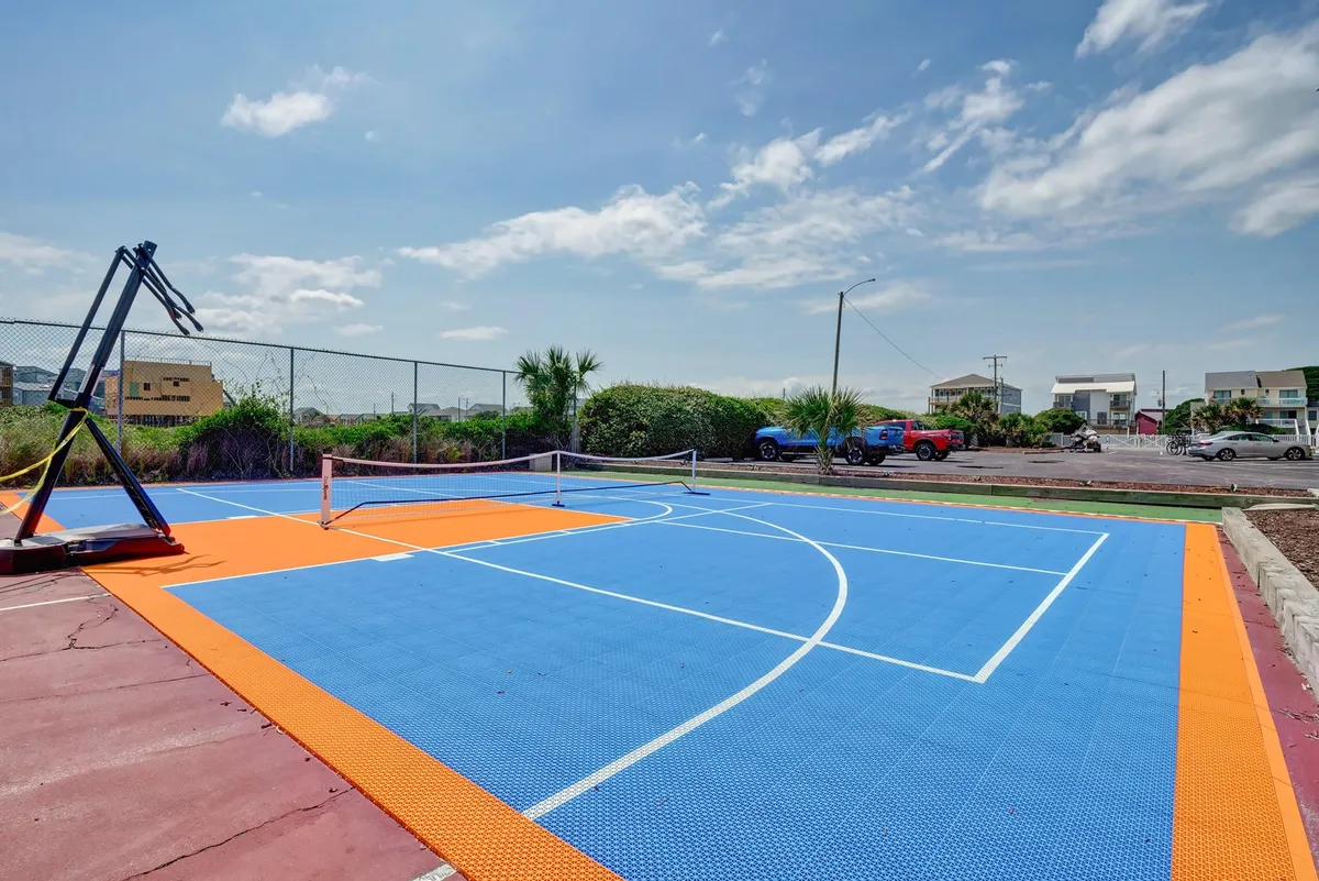 This exterior image features a vibrant sports court with both a basketball hoop and a tennis (or pickleball) net, set against a bright and inviting backdrop. The court's colorful surface and open design encourage active play and outdoor recreation.