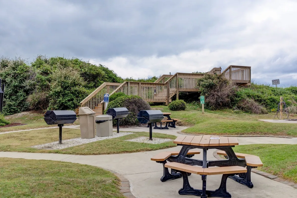 This exterior image features picnic tables and barbecue grills set on a wooden deck surrounded by greenery. The relaxed, open-air environment invites communal gatherings, outdoor meals, and opportunities for relaxing or socializing after a productive workday.
